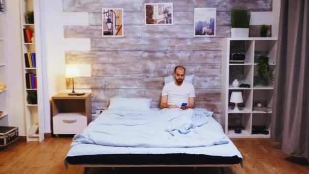 Blanke man in bed lezen op zijn telefoon — Stockvideo