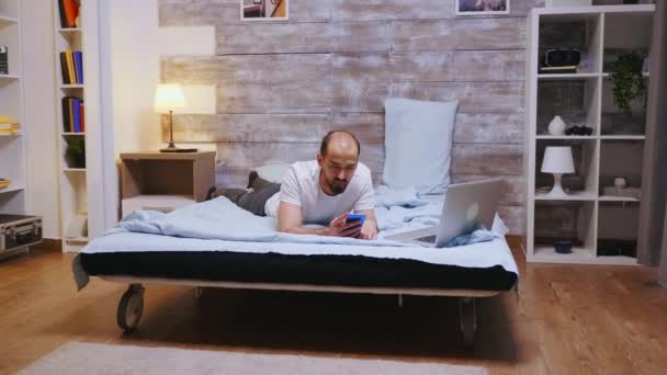 Hombre en pijama navegando en smartphone — Vídeos de Stock