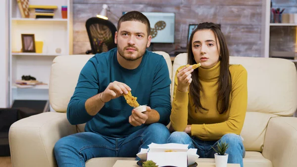 Mladý pár sedí na gauči jíst smažené kuře — Stock fotografie