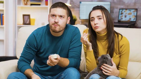 Geconcentreerd jong paar zitten op de bank eten gebakken kip — Stockfoto