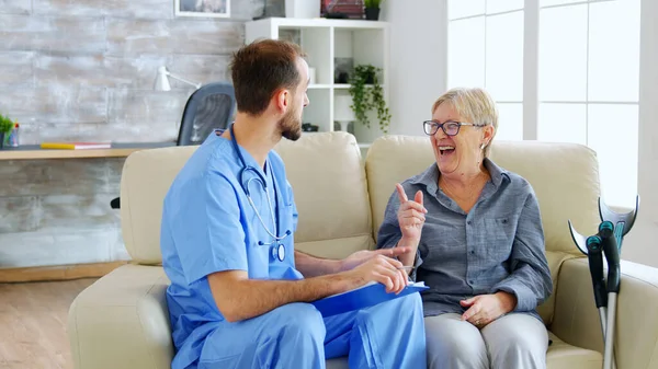 Doctor assistant taking notes on clipboard while listening to old retired woman in nursing home