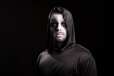 Azrail gibi giyinmiş genç adam kameraya ciddi ciddi bakıyor.