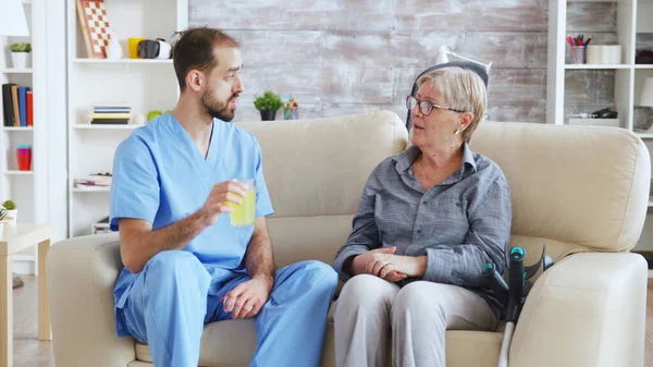 Infermiera seduto sul divano con la donna anziana dando il suo trattamento medico in casa di cura — Foto Stock