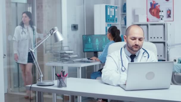 Человек врач печатает на ноутбуке в современном офисе — стоковое видео