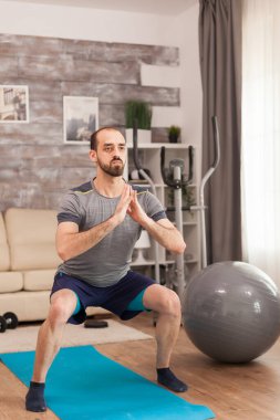 Spor kıyafetli zinde bir adam çömeliyor.