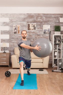Fit adam İsviçre topuyla yoga minderinde hamleler yapıyor.