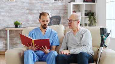 Sosyal hizmetler görevlisi huzurevindeki engelli bir adama kitap okuyor.