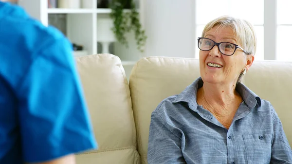Старша стара жінка сидить на дивані в будинку престарілих розмовляє з лікарем — стокове фото