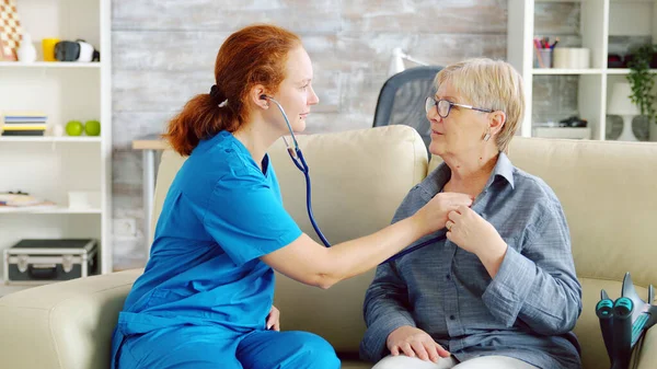 Caucasienne femme médecin dans maison de soins infirmiers écoute vieille femme battement de coeur — Photo