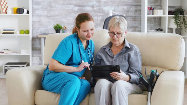 Nuse femminile aiutare anziana anziana pensionato donna come utilizzare il suo computer tablet — Foto Stock