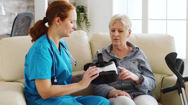 Female nurse helping senior woman to experience virtual reality