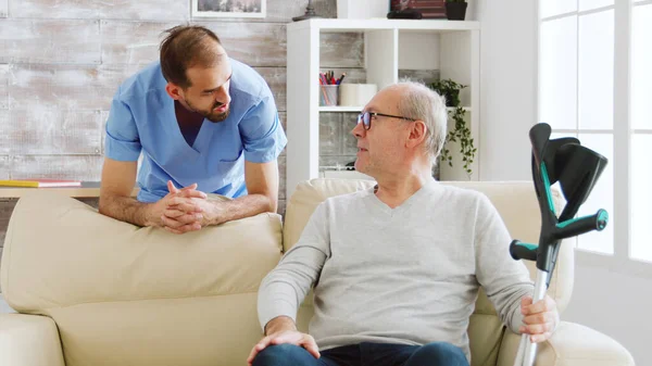 Uomo anziano avendo una conversazione con un infermiere maschio in accogliente casa di cura — Foto Stock