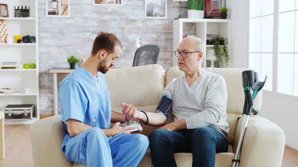 Чоловіча медсестра вимірює кров'яний тиск чоловіка пенсіонера — стокове фото