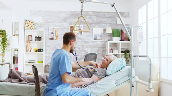 男性看護師チェックザハートビートのA病院ベッドに横たわっている病気の老婦人 — ストック写真