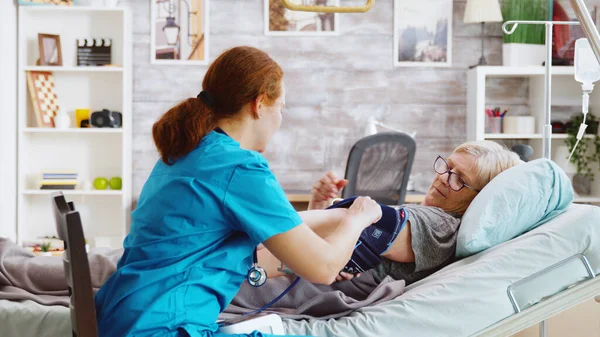 Nurse measuring blood pressure of old sick lady laying in hospital bed — Stock Photo, Image