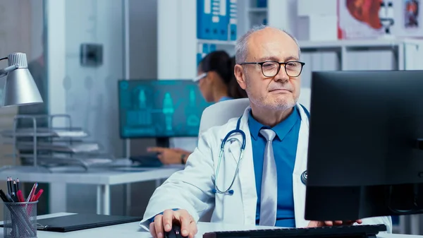 Elderly doctor working on PC — Stock Photo, Image