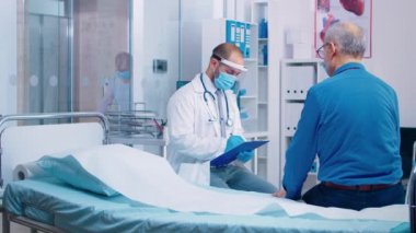 Maskeli doktor kıdemli erkek hastayla konuşuyor.