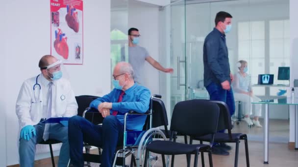Ogiltig gammal man med ansiktsmask diskuterar med läkare på sjukhus väntrum — Stockvideo