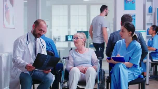 Médico con radiografía de una mujer mayor discapacitada en silla de ruedas — Vídeos de Stock