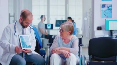 Doktor tekerlekli sandalyedeki yaşlı kadına teşhisi açıklıyor.