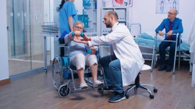 Doktor yaşlı kadına tekerlekli sandalyede yardım ediyor.