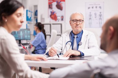 Yaşlı doktor tekerlekli sandalyedeki engelli adama bakıyor.
