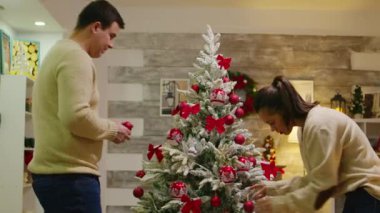 Takım elbiseli beyaz çift Noel ağacını süslüyor.