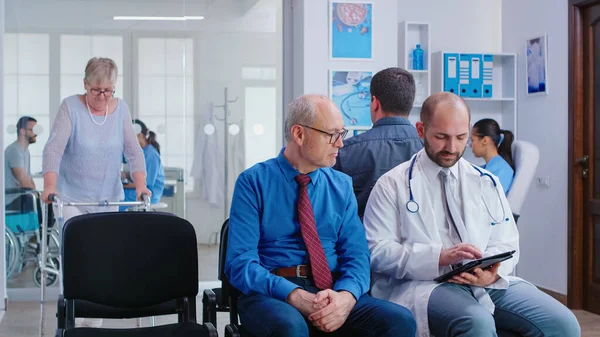 Doctor explicando los resultados de las pruebas al hombre mayor en la sala de espera del hospital — Foto de Stock