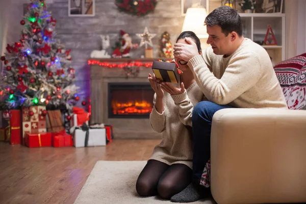 Young man covering eyes of his partner while he is giving her gift — Stock Photo, Image
