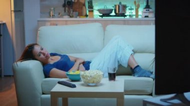 Kadın televizyon izliyor ve sıkılıyor.