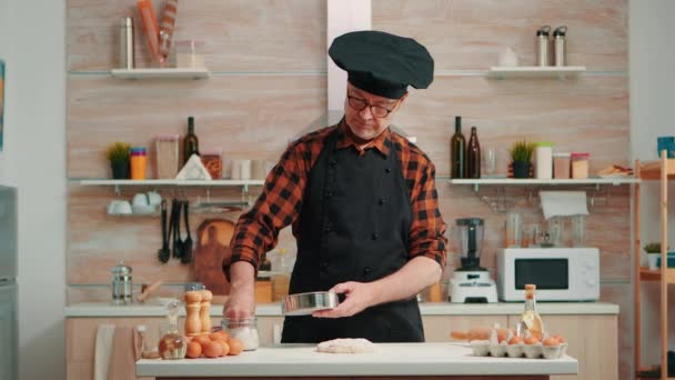 Бейкер з бонете і кухонним фартухом за допомогою металевого сито. — стокове відео