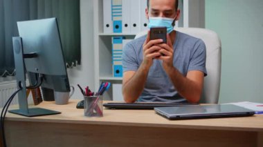 Maskeli bir ofis çalışanı telefon kullanıyor.