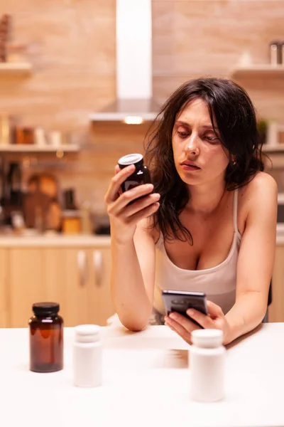 Niezdrowa kobieta patrząc na butelkę tabletek — Zdjęcie stockowe