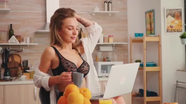 Frestande kvinna i sexiga underkläder använder laptop på morgonen i köket — Stockvideo