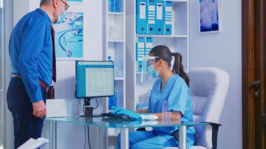 Hastane resepsiyonundaki hemşire kıdemli hastayı selamlıyor.