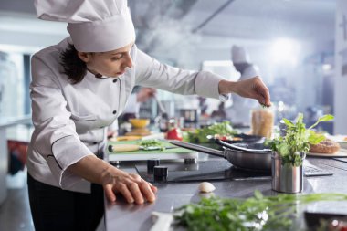 Kadın şef fırının tepesindeki tabağın üzerine taze biberiye serpiyor, yemek tabaklarına ve aromaya odaklanıyor. Taze malzemelerin hazırlanması, aşçılık çalışma alanında bir bitki karışımı sağlanması.