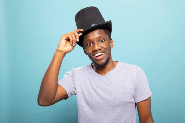 Kostümlü, gülümseyen Afro-Amerikan bir adam gösteriye hazırlanıyor. Neşeli siyah büyücü sıradan bir tişörtle silindir şapkasını düzeltirken klasik bir sihirbazlık gösterisine hazırlanıyor..