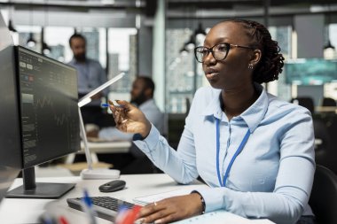 Risk analisti piyasa dalgalanmalarını tespit etmek için canlı piyasa faaliyetlerini izliyor. Portföy performans raporlarını inceleyen Afrikalı Amerikalı kadın potansiyel mali riskleri kontrol ediyor.