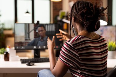 Siyah kadın sanal toplantı için masaüstü bilgisayarını kullanıyor. Evden bir iş danışmanıyla pazarlama stratejilerini tartışıyor. Erkek danışman ekranda görünüyor, odaklanmış girişimciye stratejik içgörüler sunuyor