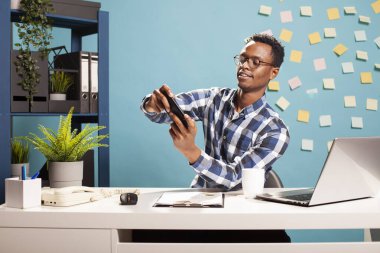Afrikalı Amerikalı erkek analist video oyunları için cep telefonu kullanıyor, pazarlama şirketinde iş ve eğlence dengesini sağlıyor. Genç işadamı masasında oturmuş, cep telefonuyla oyun oynuyordu..