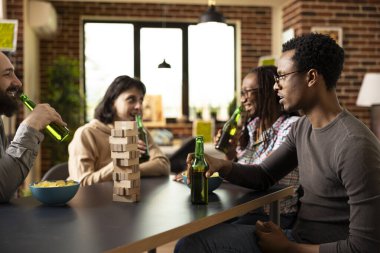 Bir grup çok ırklı arkadaş masanın etrafında oturmuş, samimi tuğla duvar odasında kahkaha, içki ve atıştırmalıkları paylaşıyorlardı. Neşeli yoldaşlar rahatlar ve sıcak ve samimi bir şekilde kaynaşırlar..