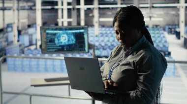 Veri merkezi yönetimi, sondaj sistemleri incelemesi sırasında dizüstü bilgisayarla Al 'ın gösterge panelini kontrol ediyor. Sunucu merkezindeki Afrikalı Amerikalı kadın güvenilir performansı kontrol etmek için yapay zeka araçlarını defterde test ediyor