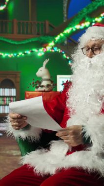 Noel Baba kılığındaki dikey videocu çocuklardan gelen mektupları okurken neşeli tavırlar sergiliyor. Kırmızı Noel Baba kostümü giyen kişi çocukların Noel dileklerini okumak için neşeli bir ortam yarattı.