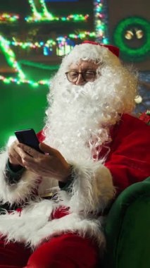 Dikey video Noel Baba hediye isteyen çocuklara cevap veriyor, akıllı telefon ekranında kaydırıyor. Noel Baba kılığına girmiş biri çocuklara Noel için cep telefonu kullanarak ne istediklerini soruyor.
