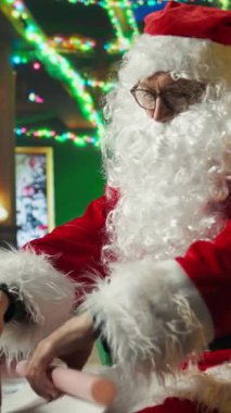 Noel Baba kış sezonunda Noel Baba 'nın dikey gösterisi bayram neşesi yayıyor, hediye paketliyor. Noel Baba gibi giyinmiş bir adam neşeli bir ortam yaratıyor, hediye yapmak için ambalaj kağıdı kullanıyor.