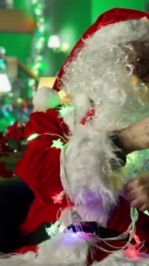 Noel Baba 'nın dikey videosu, Noel' de atölyeyi dekore ederken ışıklara dolandı ve ailelerin ziyaretine hazırladı. Noel süsleri yaparken kostüm giymiş bir adam Noel ışıklarında düğümlendi.