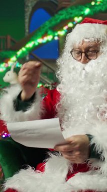 Noel Baba rolünü oynayan dikey videolu yaşlı adam çocuklardan gelen mektupları okumak için gözlük takıyor. Noel Baba kıyafeti giyen bir aktör süs odasında çocuklardan gelen mektupları okuyor.