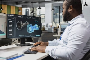 Yeşil teknoloji şirketinde bilgisayar yazılımı kullanan teknisyen sürdürülebilirlik ölçümlerini geliştirmek için türbin bileşenlerini analiz ediyor. Afrika kökenli Amerikalı adam emisyonları azaltmak için türbin parçalarına bakıyor