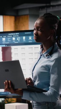 Dikey Video Siyah kadın geliştirici 3D modellerle imar düzenlemelerini gözden geçiriyor, sürdürülebilir konut geliştirme için ana planı akıllı şehir altyapısıyla uyumlu olan konut projesi