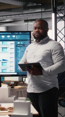 Dikey Video Emlak Yatırım Geliştiricisi, modern bir ofisteki inşaat alanının planlarını ve yerleşim planlarını kontrol ediyor. İkamet geliştirme projesi için imar yönetmelikleri analiz ediliyor